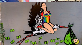 Elly Schlein cavalca una cicogna in versione arcobaleno: il murale sulla maternità surrogata spuntato a Milano nel giorno del Pride – Foto e video